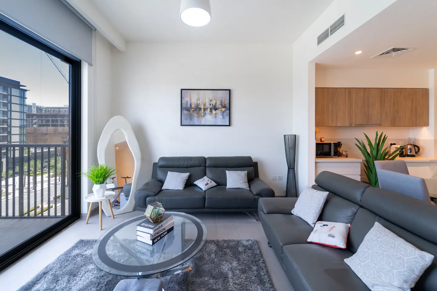 Living room with gray sofas, glass table, and a view from a large window. Modern decor with white walls and wood cabinets.