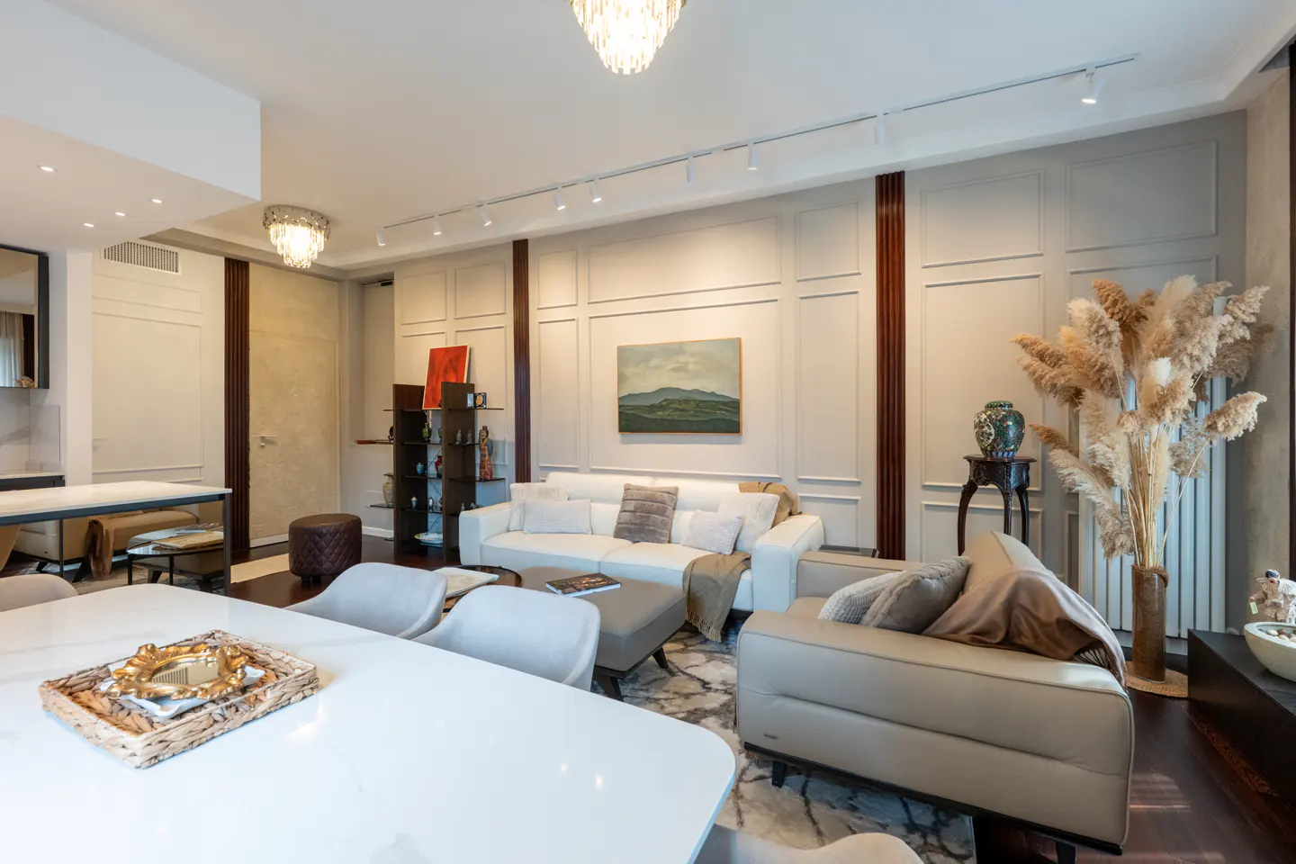 Modern living room with white sofa, beige armchair, marble dining table, and decorative pampas grass in a bright interior.