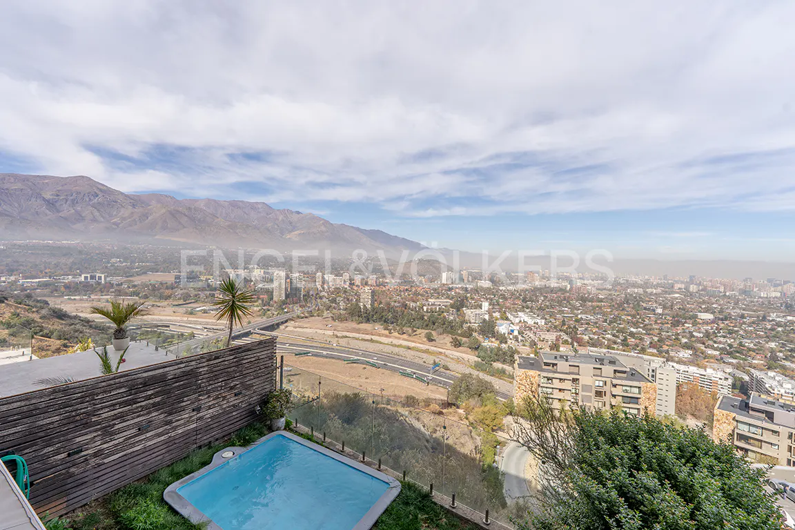 High-angle view of a small pool on a wooden deck overlooking a sprawling city with mountains in the background.