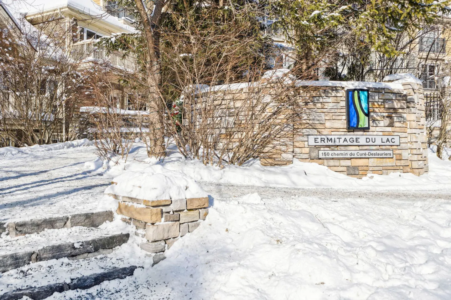 Stone sign for "Ermitage Du Lac" with address, surrounded by snow-covered ground and bare trees in winter.