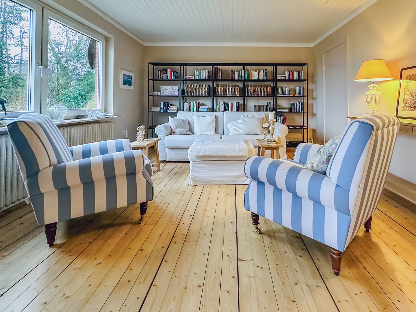 Living room with two blue and white striped armchairs facing a white sofa and a black bookshelf.