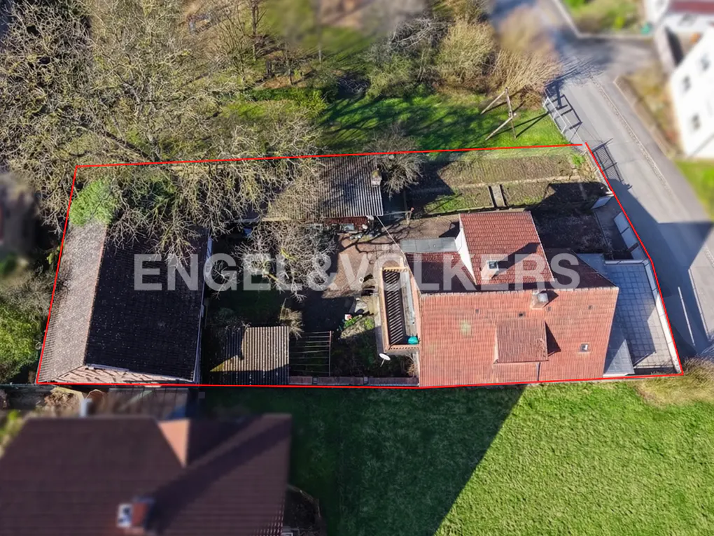 Aerial view of a property with a red outline, featuring a house with a red tile roof and a green lawn.