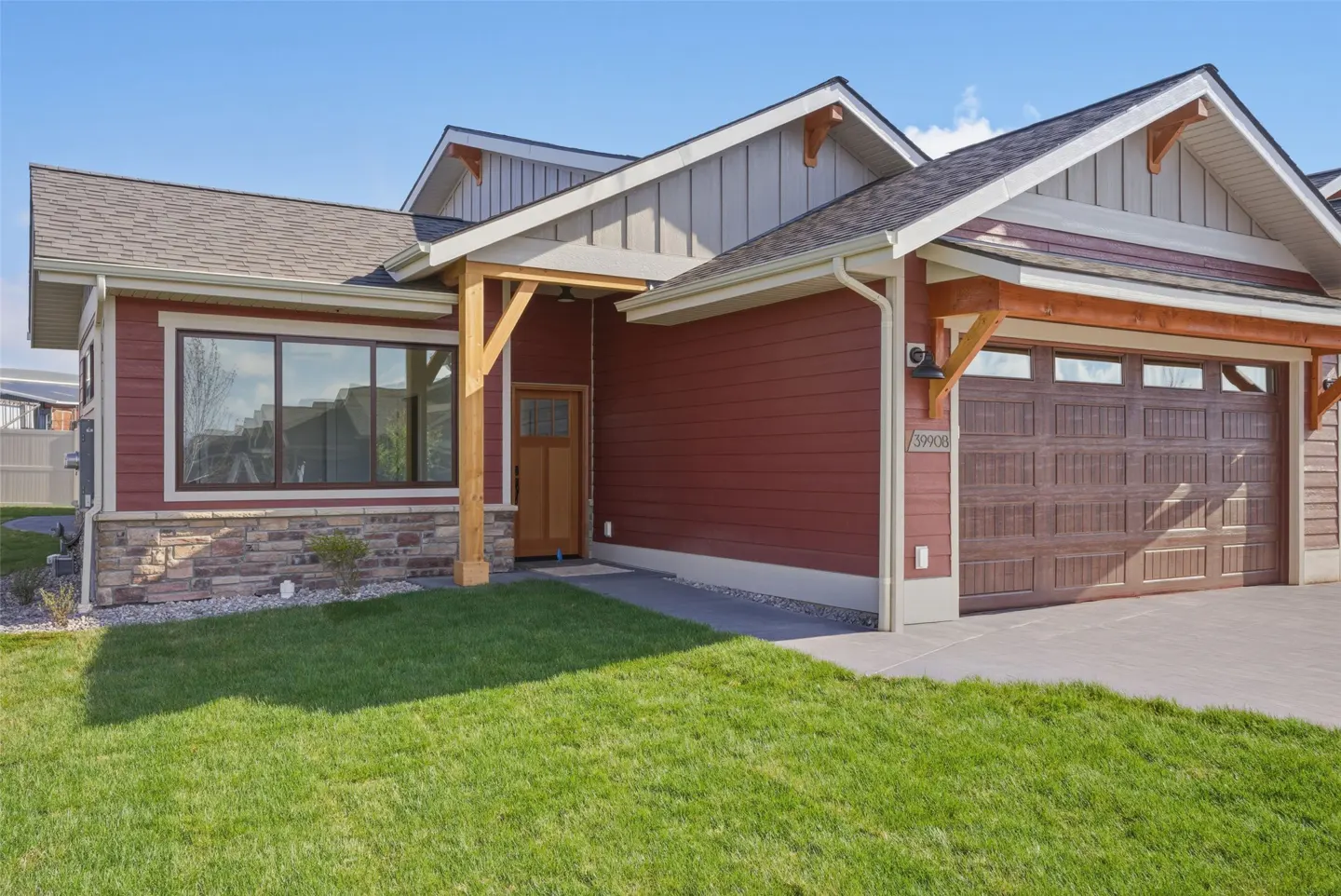 A single-story house with red siding, a brown garage door, and a green lawn under a blue sky.