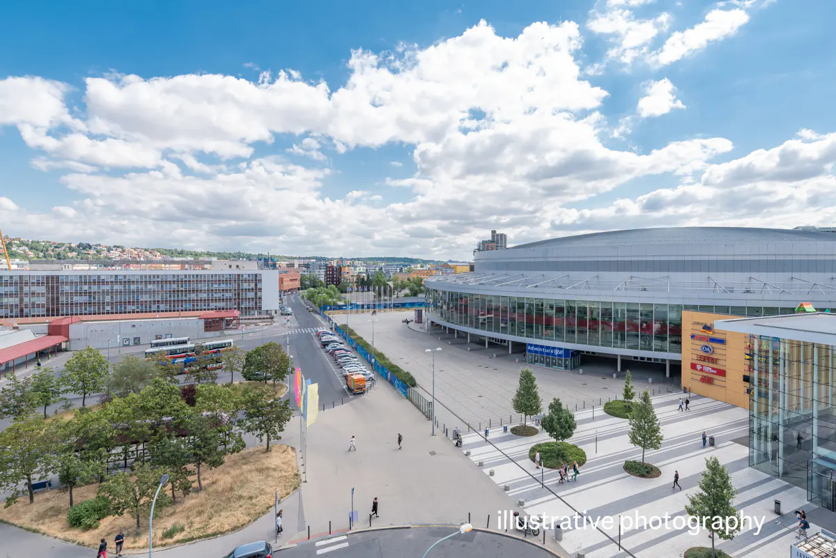 Wide shot of a city with a large arena, buildings, trees, and a blue sky with white clouds.