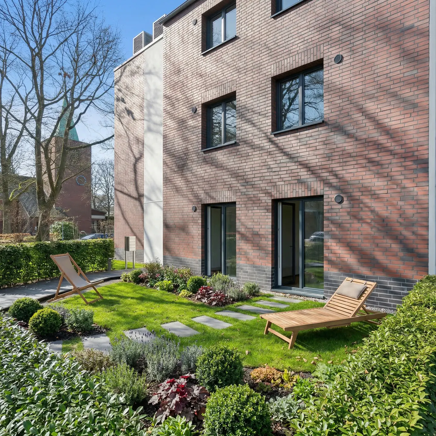 Brick building with black framed windows and doors, a green lawn, and two wooden lounge chairs.