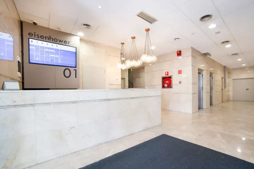 Modern lobby with marble reception desk, digital directory, and globe pendant lights. Elevators are visible in the background.