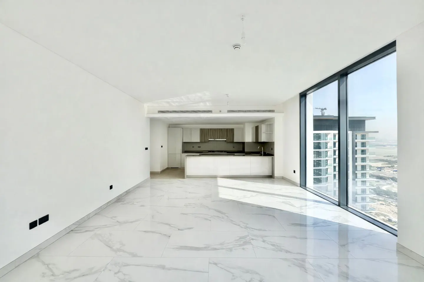 Bright, empty apartment with white walls, marble floors, and a modern kitchen. Large windows offer a city view.