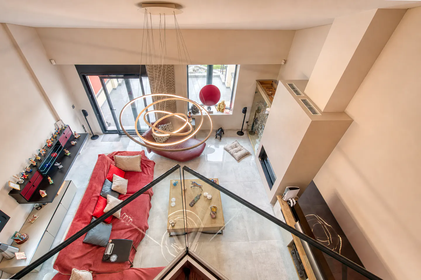 High-angle view of a modern living room with a red sofa, a wooden coffee table, a fireplace, and a circular chandelier.