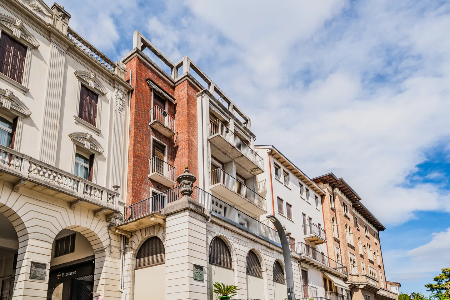 Row of buildings with arched entryways and balconies, under a blue sky with clouds.