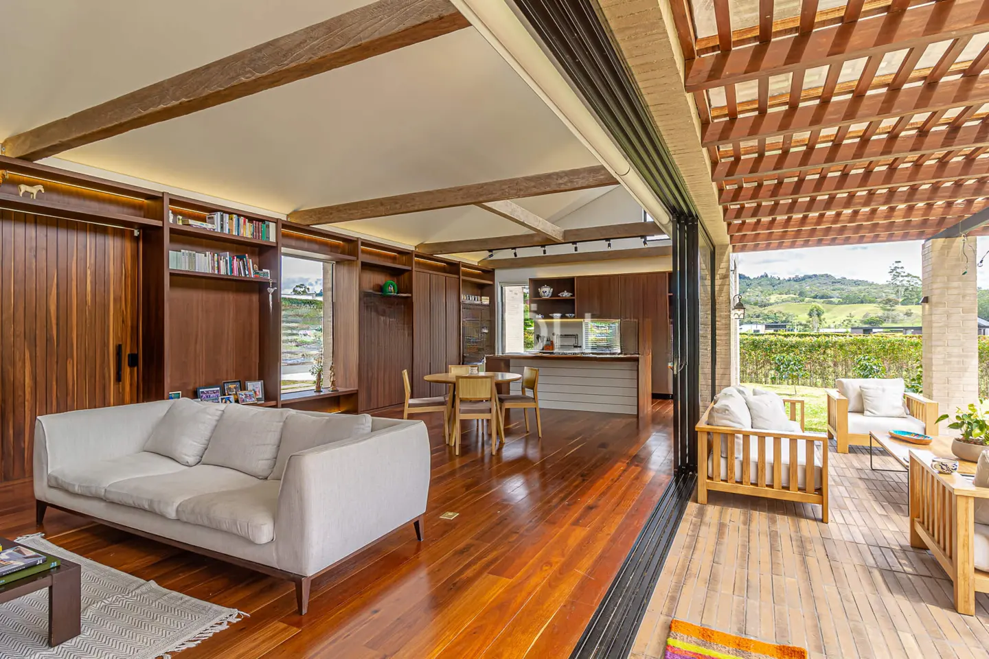 Open-concept living room with wood floors, white sofa, and built-in shelves. Patio with wood furniture and mountain view.