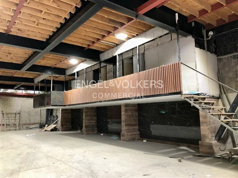 Unfinished commercial space with a wooden ceiling, black steel beams, and a second-floor balcony with the Engel & Volkers logo.