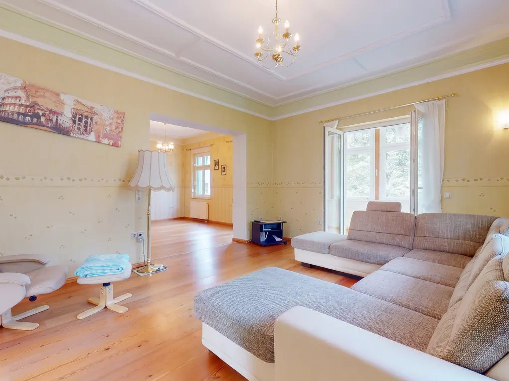 Spacious living room with yellow walls, hardwood floors, a large grey sectional sofa, floor lamp, and an adjacent room.