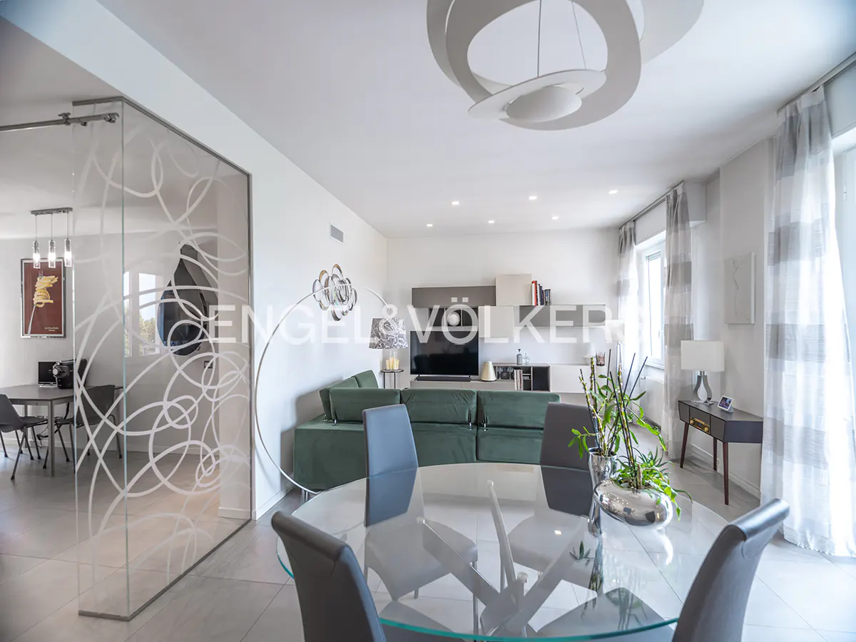 Bright, modern living space with a glass dining table, green sofa, and decorative glass wall. Neutral tones and natural light create an airy feel.