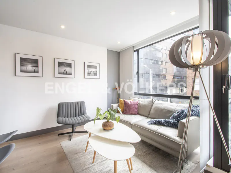 Bright living room with a gray sofa, two-tiered white table, gray chair, and a modern floor lamp by a large window.