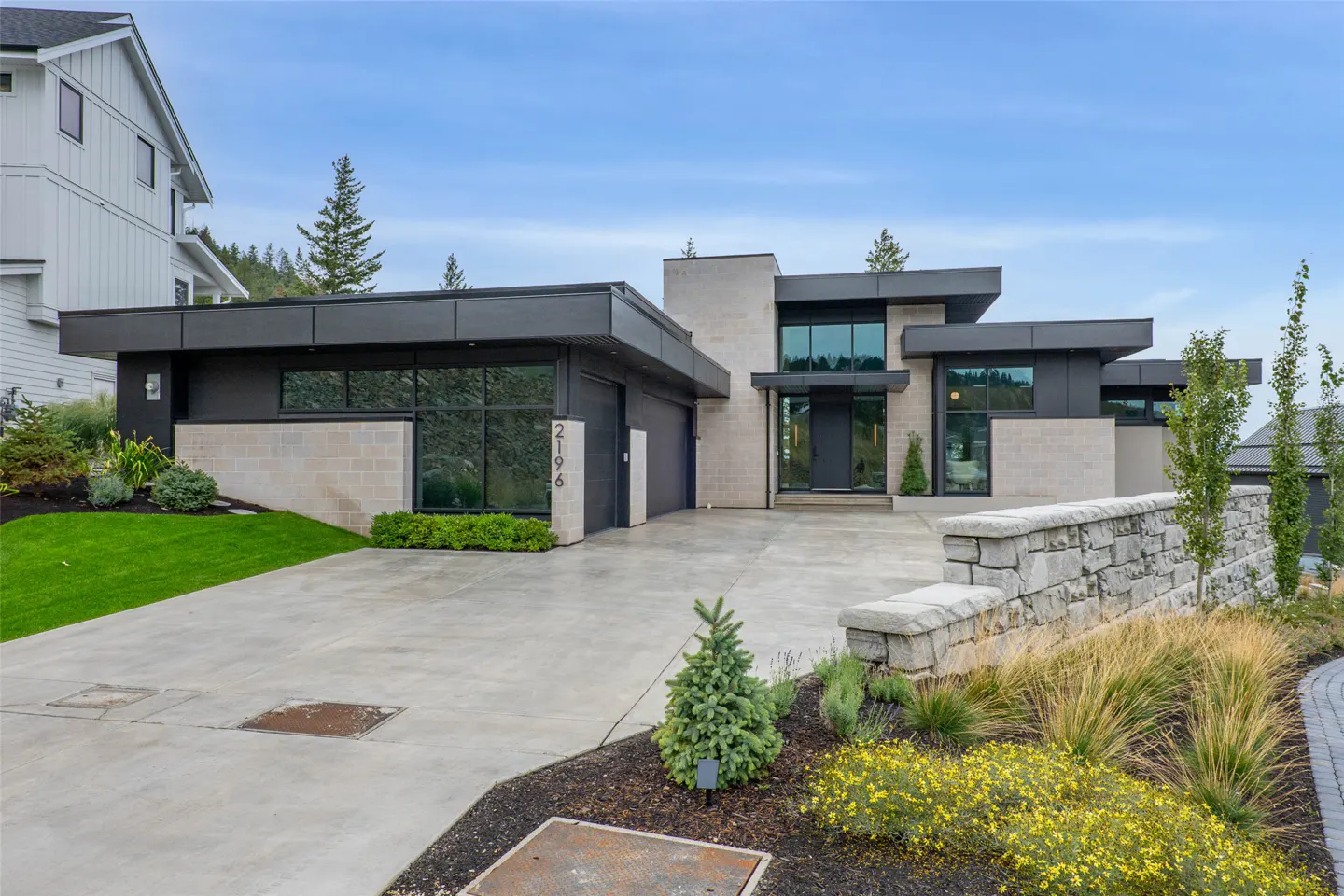 Modern single-story home with black trim, light stone accents, a concrete driveway, and landscaped front yard.