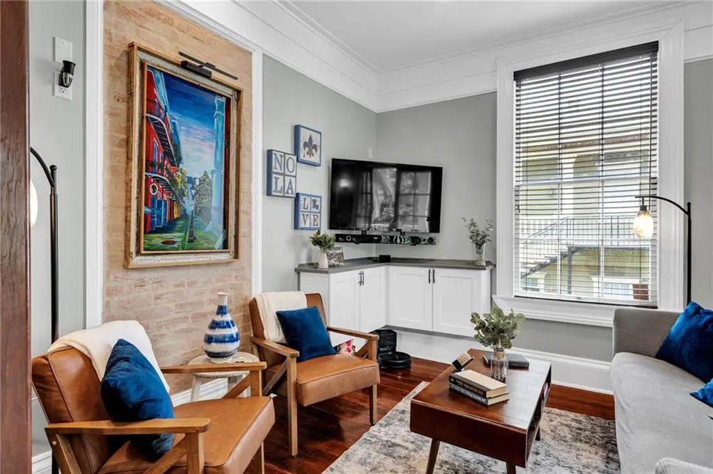 Living room with two leather armchairs, a coffee table, a brick accent wall with art, and a corner TV unit.