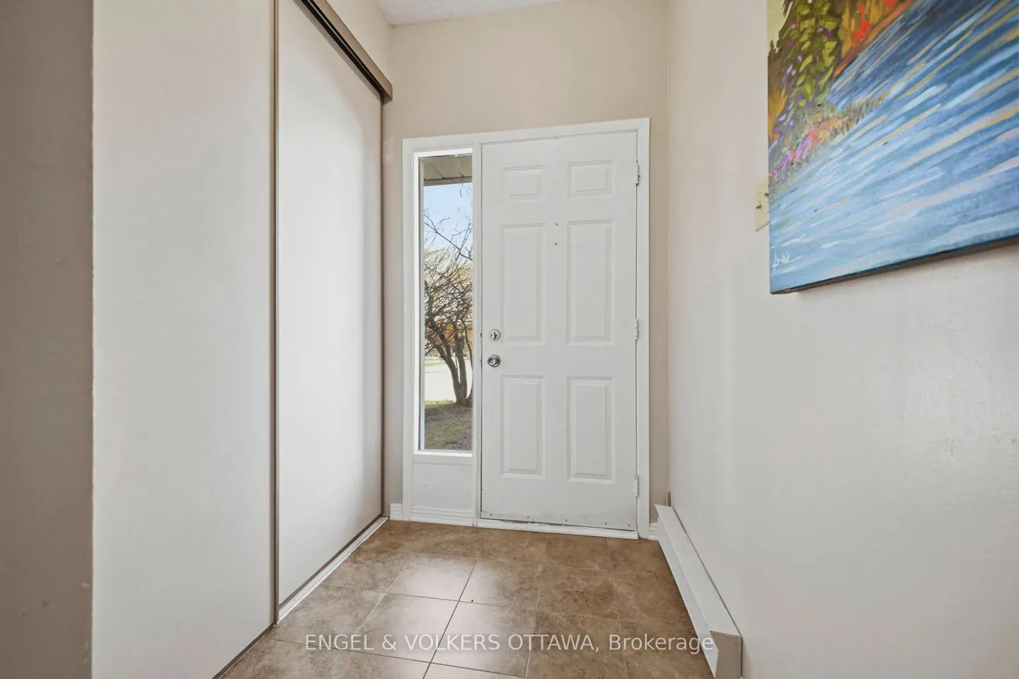 Entryway with white door, sidelight, and closet. Brown tile floor and a painting of a river on the wall.