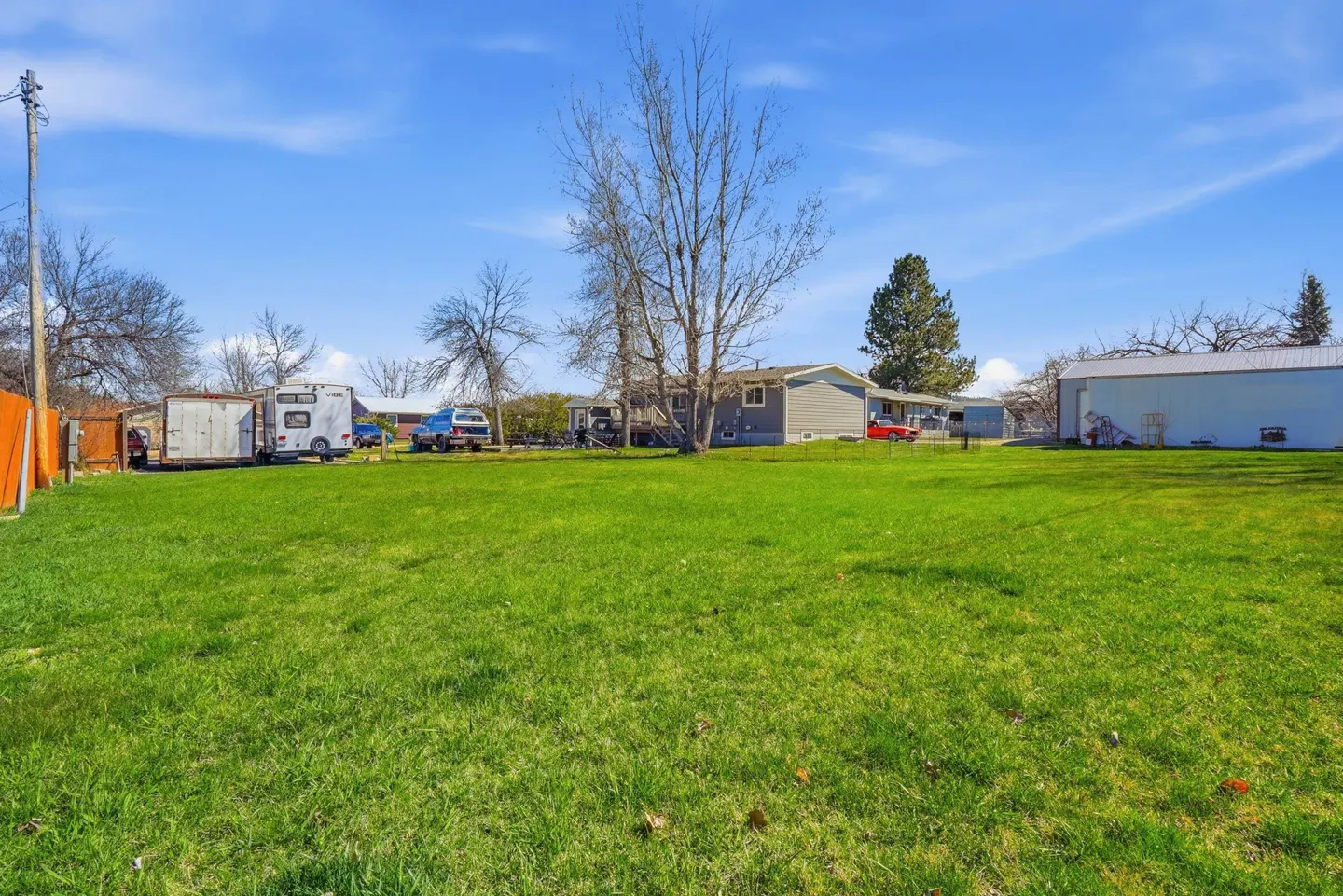 A large green lawn with a house, trailer, and vehicles in the background under a blue sky.