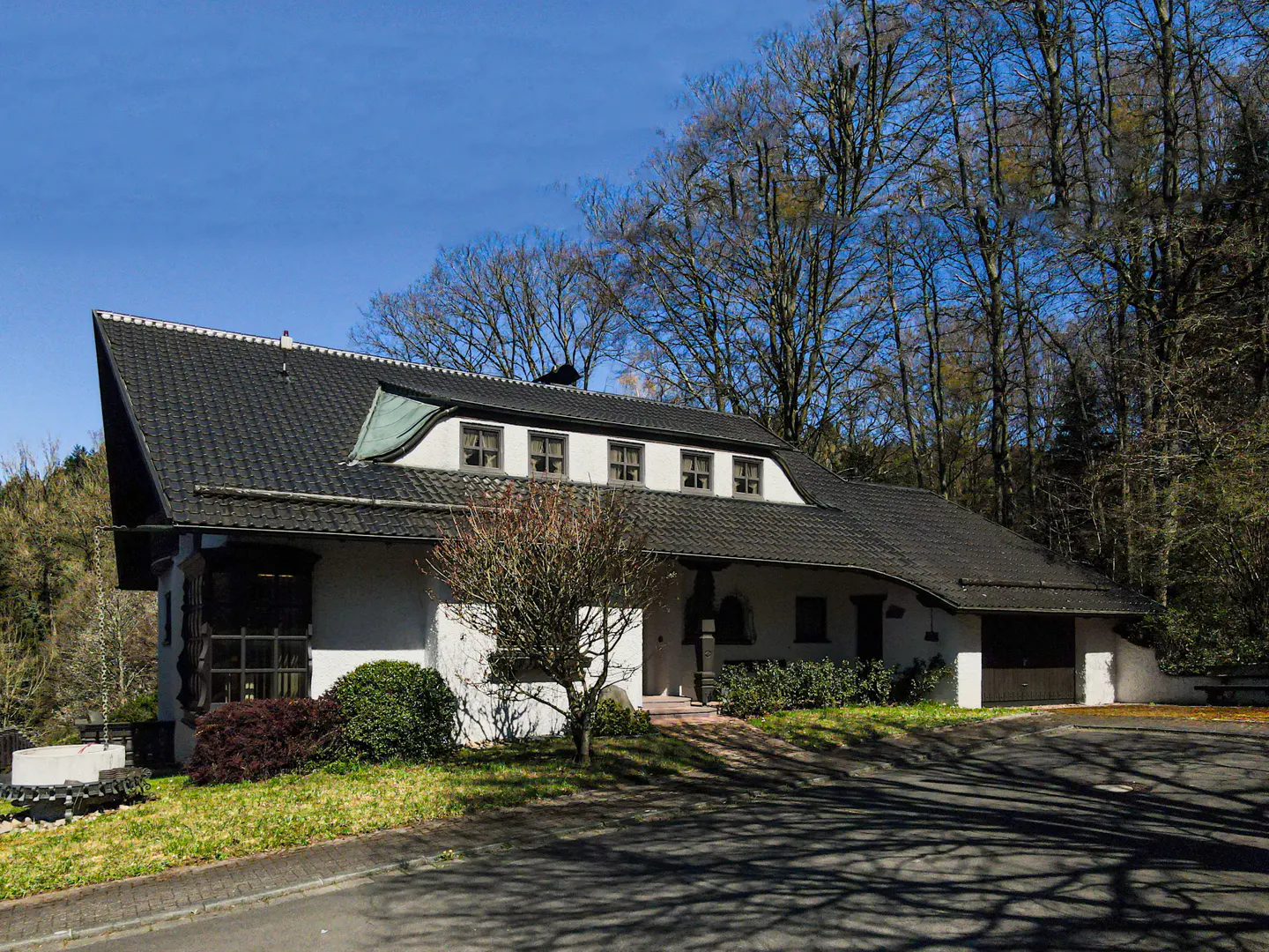 A white house with a black roof sits nestled among trees under a blue sky.
