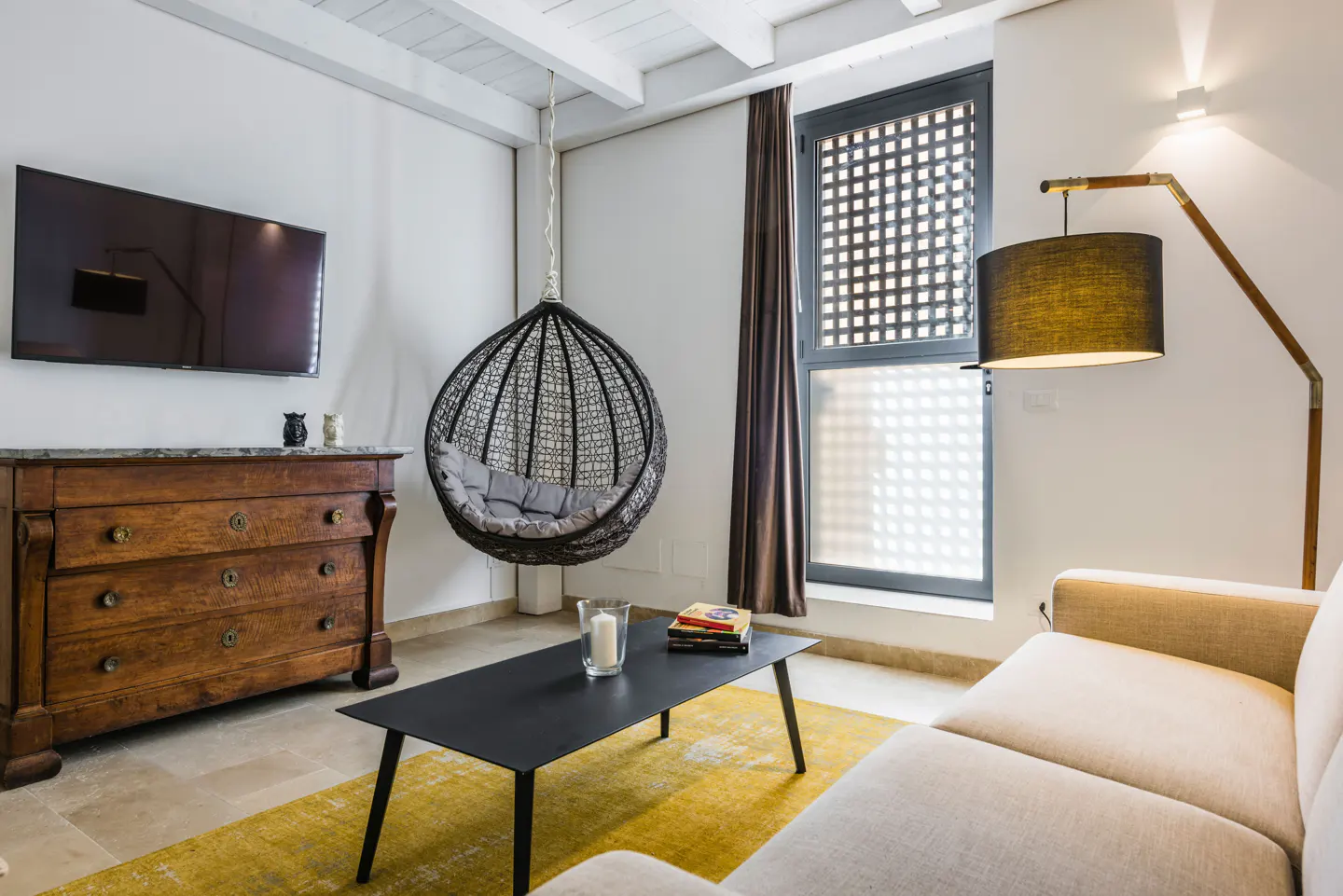 Living room with a hanging chair, black table, and a wooden dresser with a TV on top. A yellow rug is on the floor.