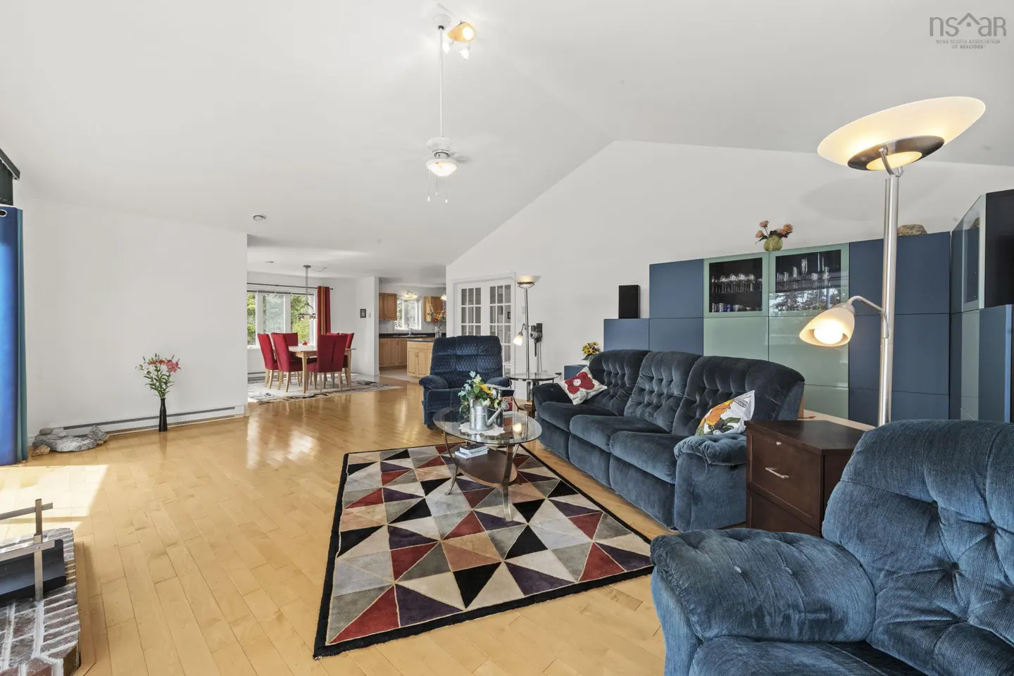 Spacious open-concept living room with hardwood floors, a blue sofa, matching recliner, and a geometric patterned rug.