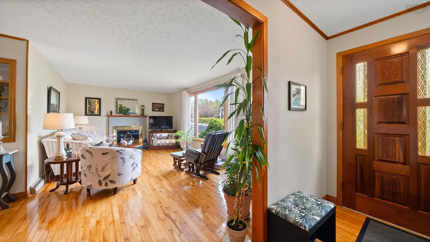 A bright living room with hardwood floors, floral armchairs, and a wooden front door with glass panels.
