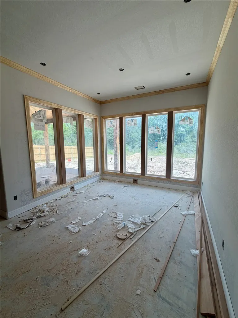 Unfinished room with light gray walls, wood trim, and large windows overlooking a construction site with debris on the floor.