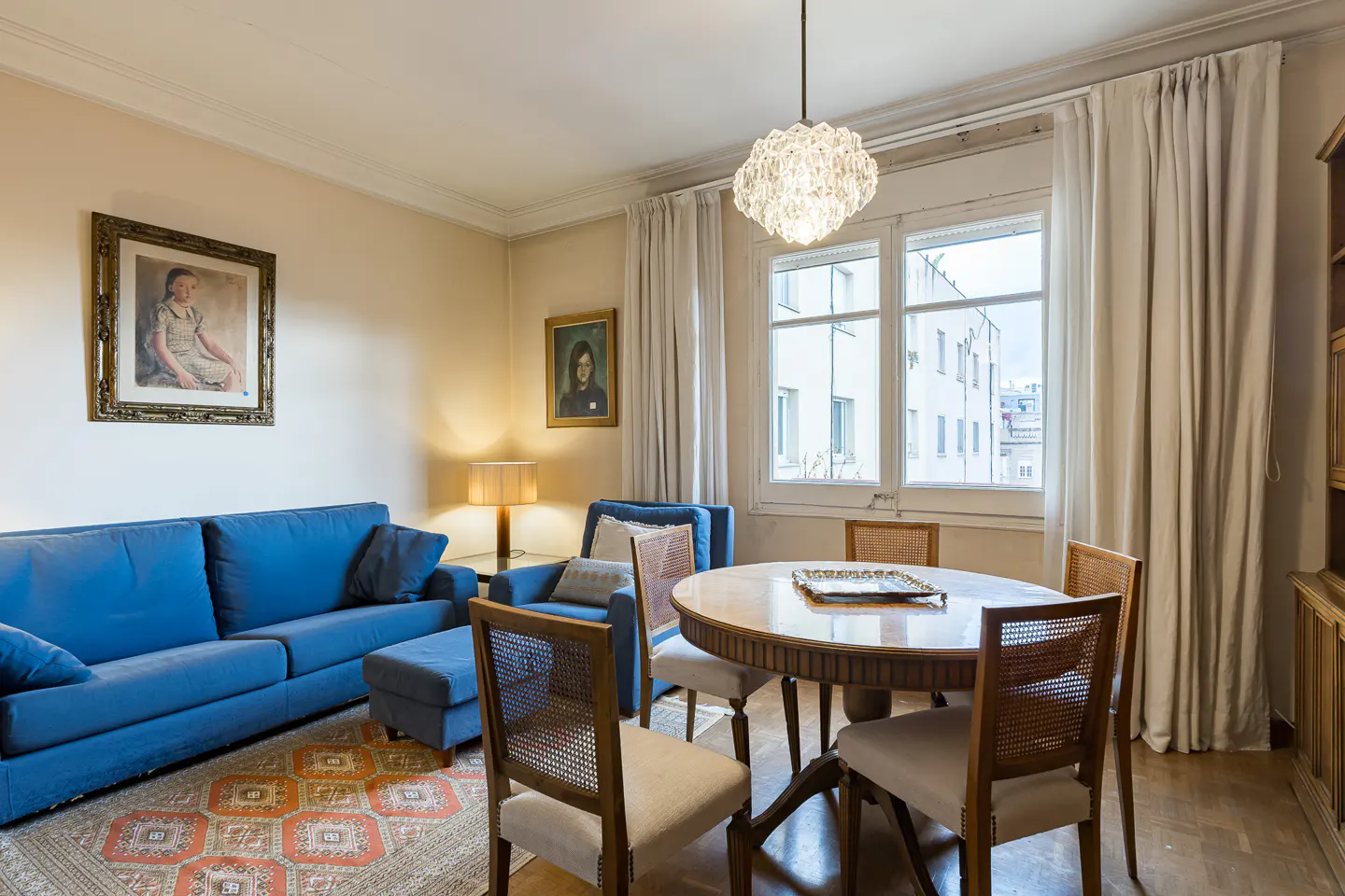 Living room with a blue sofa, matching armchair, round wooden dining table with four chairs, and a patterned area rug.