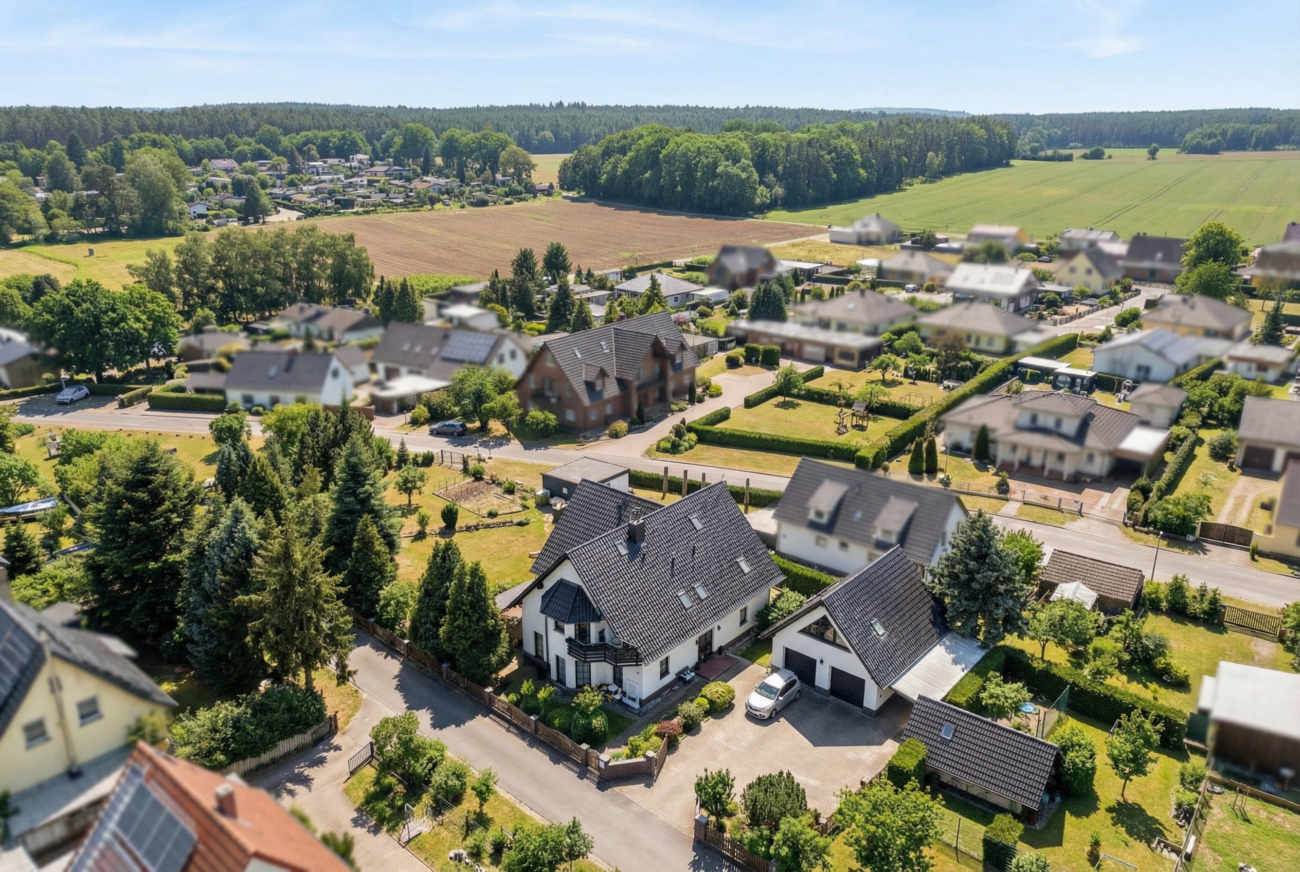 Aerial view of a suburban neighborhood with houses, trees, and fields in the background.