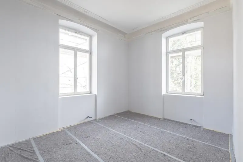 Bright, empty room with white walls, two windows, and gray floor covering.