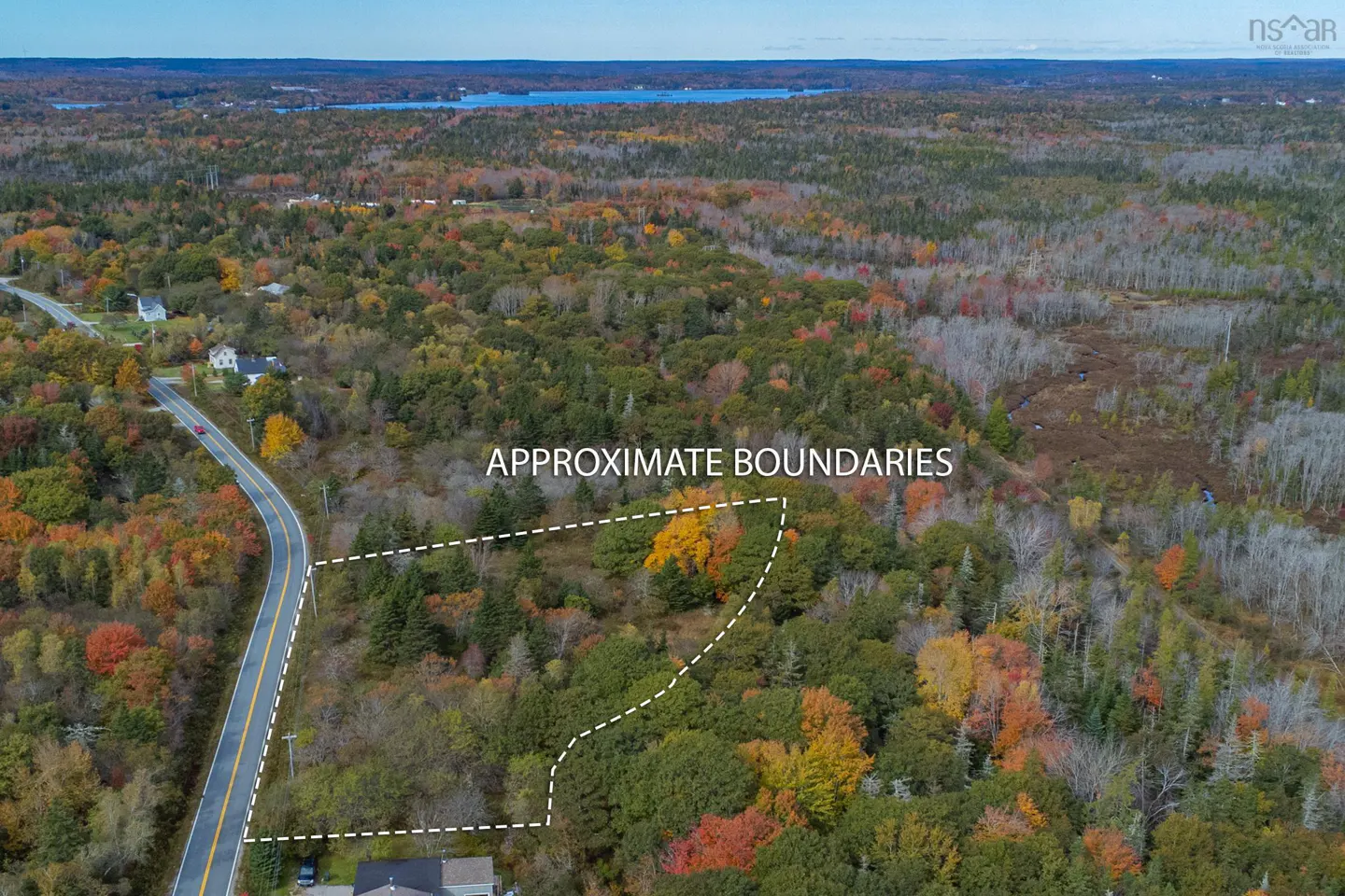 Aerial view of wooded property with approximate boundaries outlined in white. A road runs along one side. Autumn foliage colors the trees.