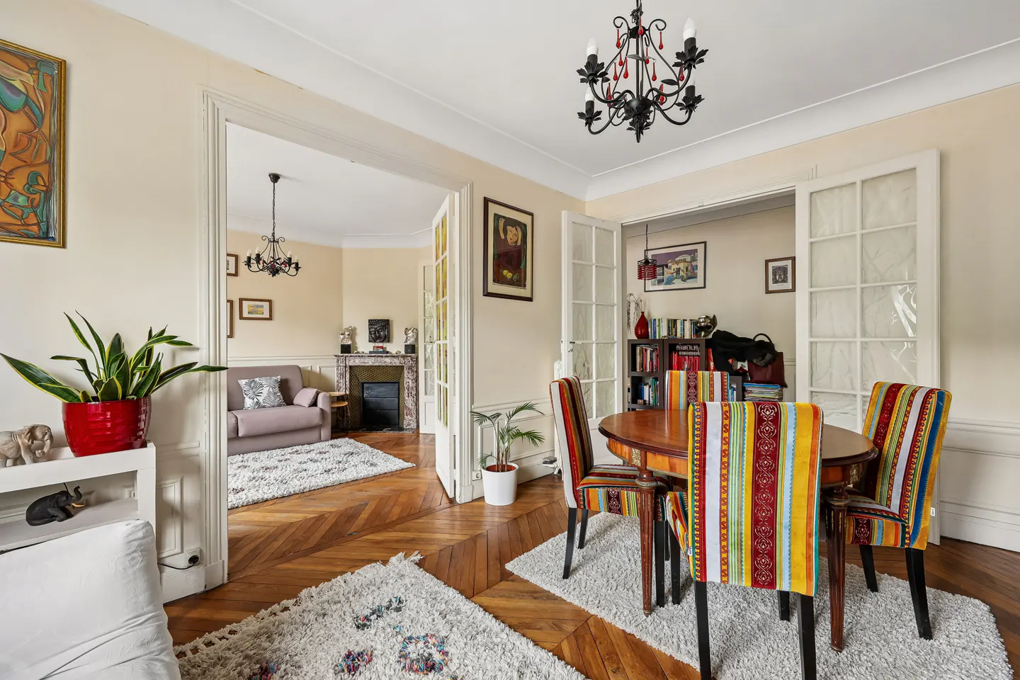 A bright, airy room with hardwood floors, a dining table with colorful chairs, and a view into a living room with a fireplace.