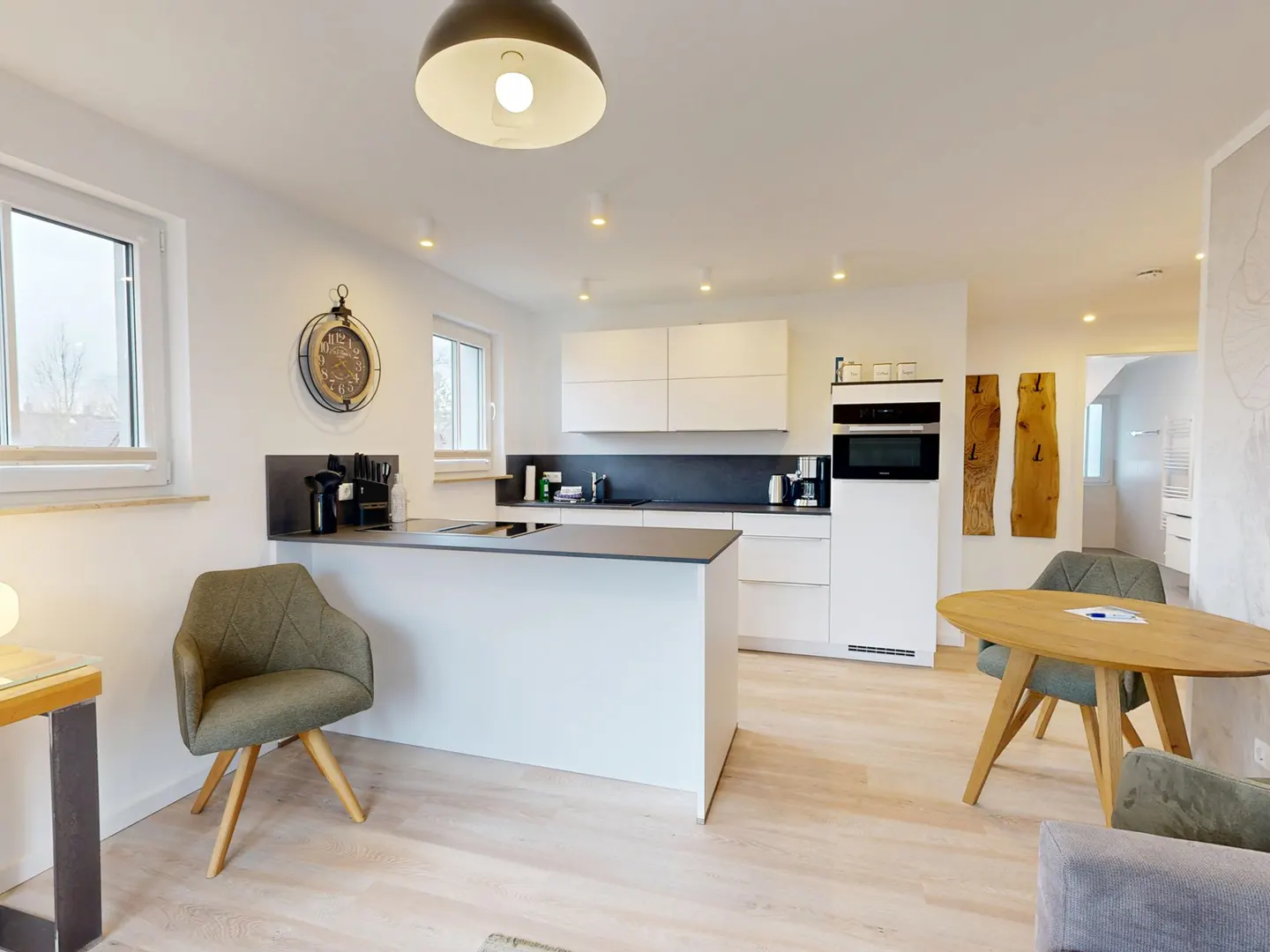 Bright, modern kitchen with white cabinets, a gray countertop island, and light wood floors. A round wooden table and green chairs sit nearby.