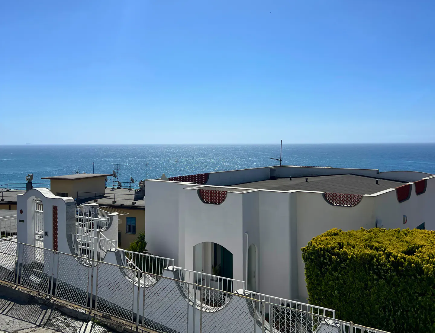 Ocean view from a white building with a decorative fence. Blue sky and water.