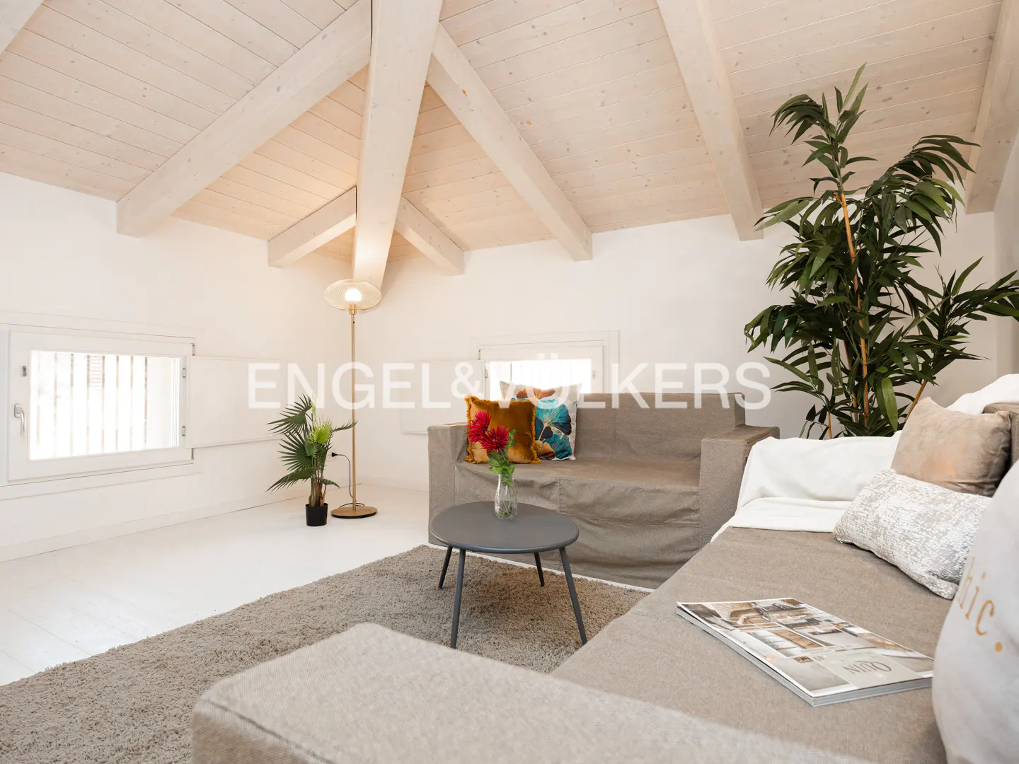Attic living room with white vaulted ceilings, beige sofa, round coffee table, floor lamp, and a large potted plant.