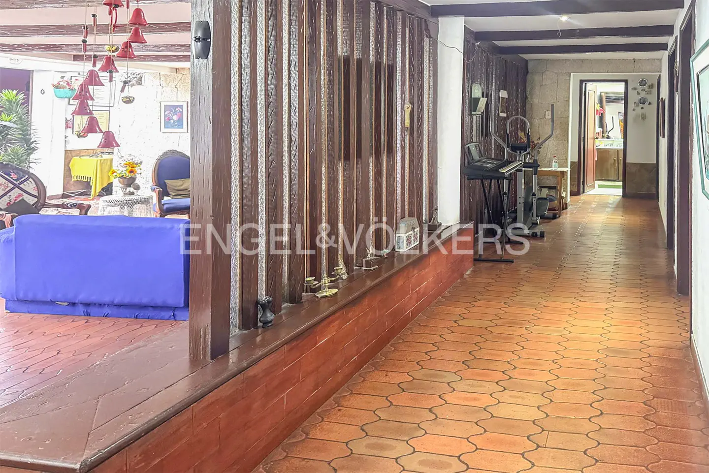 Interior view of a home with terracotta tile flooring, a blue sofa, and a hallway with exercise equipment.