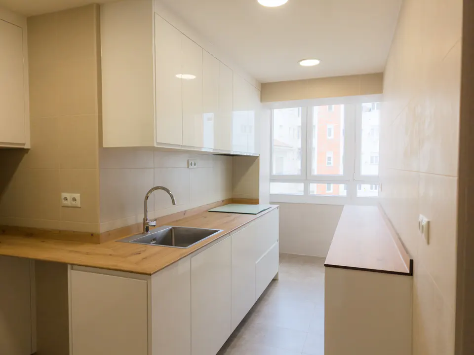 Bright kitchen with white cabinets, wood countertops, and stainless steel sink. A large window provides natural light.