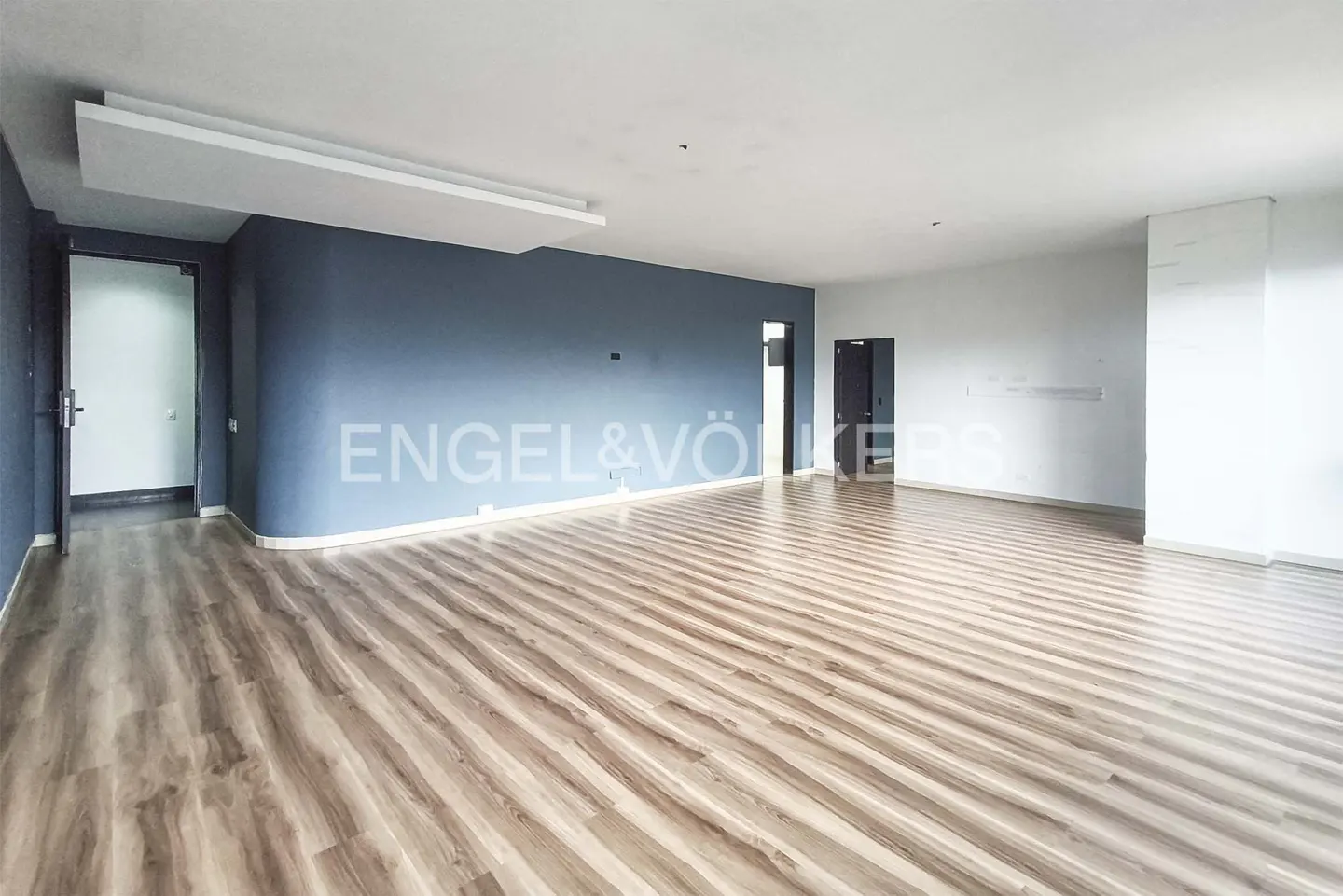 Empty room with wood floors, blue accent wall, and white walls. Engel & Völkers logo on the blue wall.