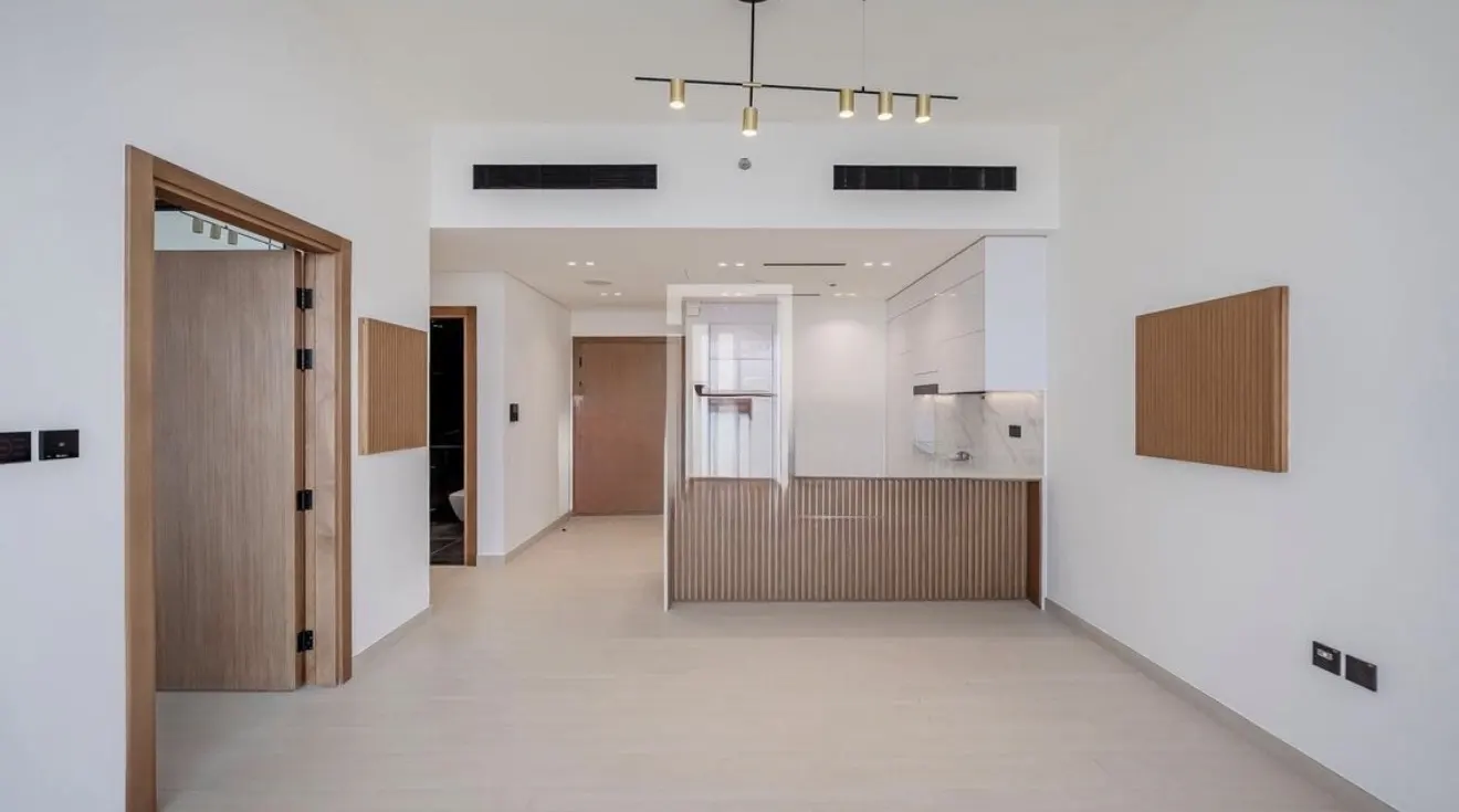 An interior view of a modern apartment with white walls, light wood doors, and a kitchen area with marble countertops.