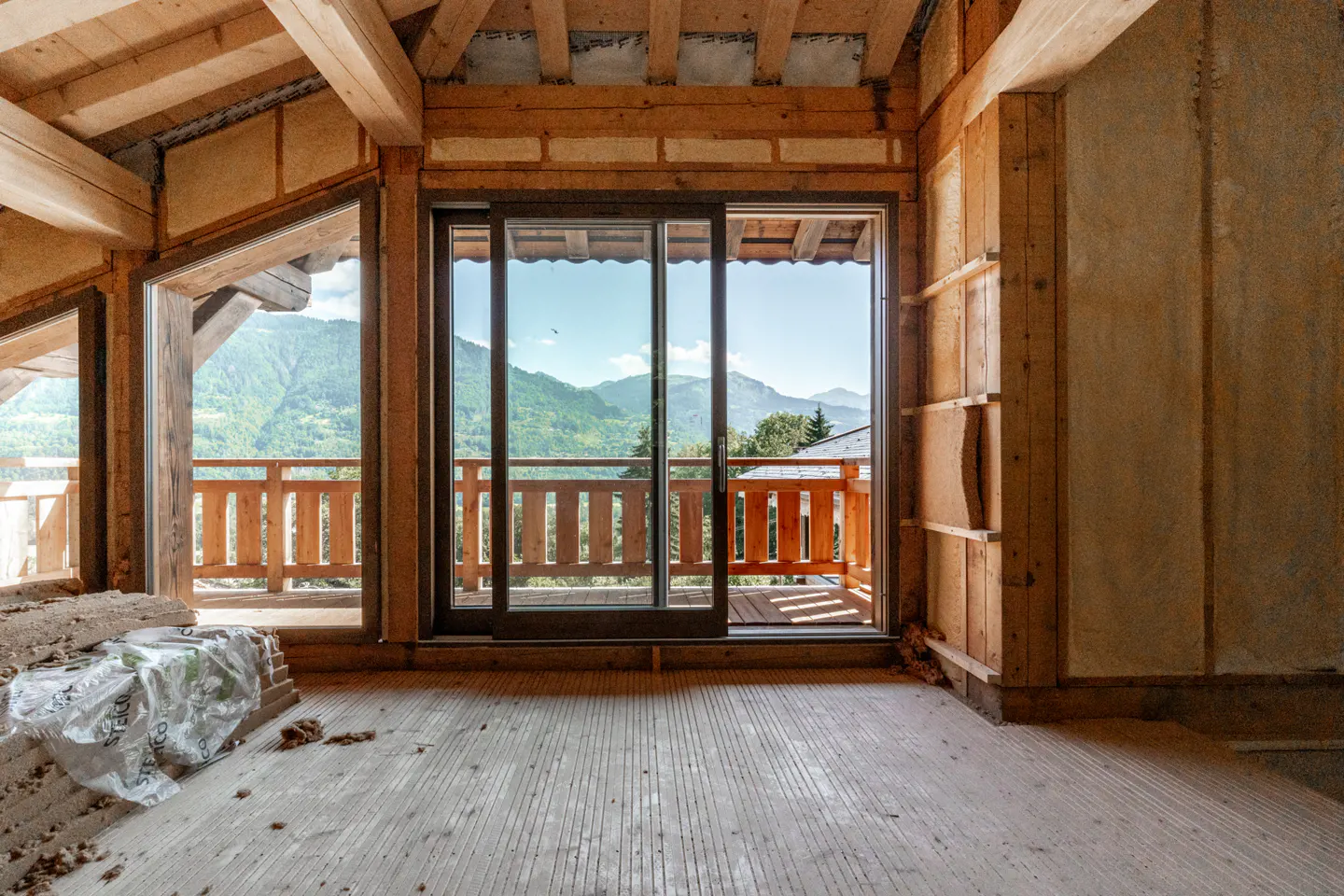 Unfinished room with wood beams, walls, and floor. Sliding glass doors open to a balcony with mountain views.