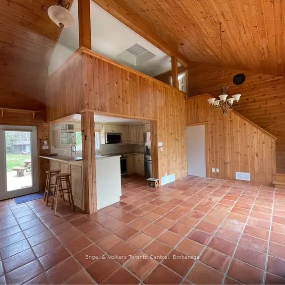 Open-concept living space with wood-paneled walls, terracotta tile floors, and a kitchen with a breakfast bar.