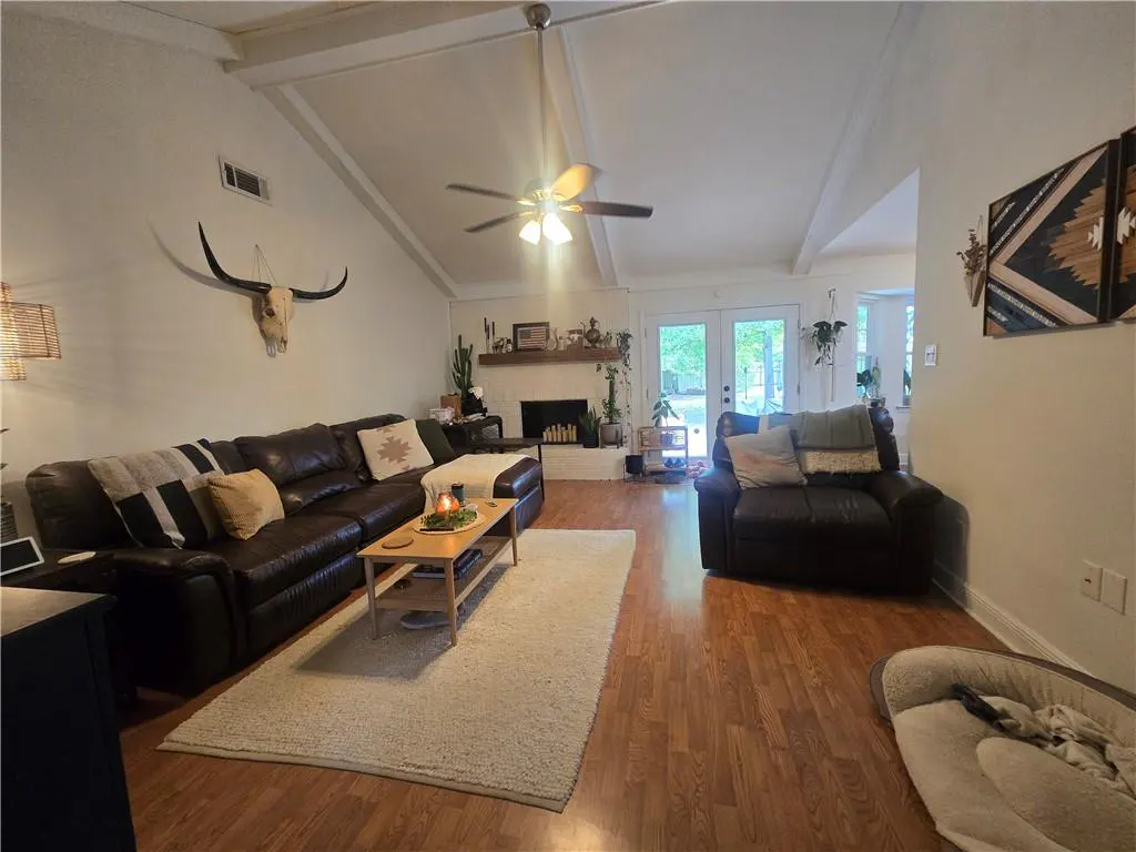 Living room with brown leather sectional, chair, wood floors, and white rug. A bull skull hangs above the sofa.