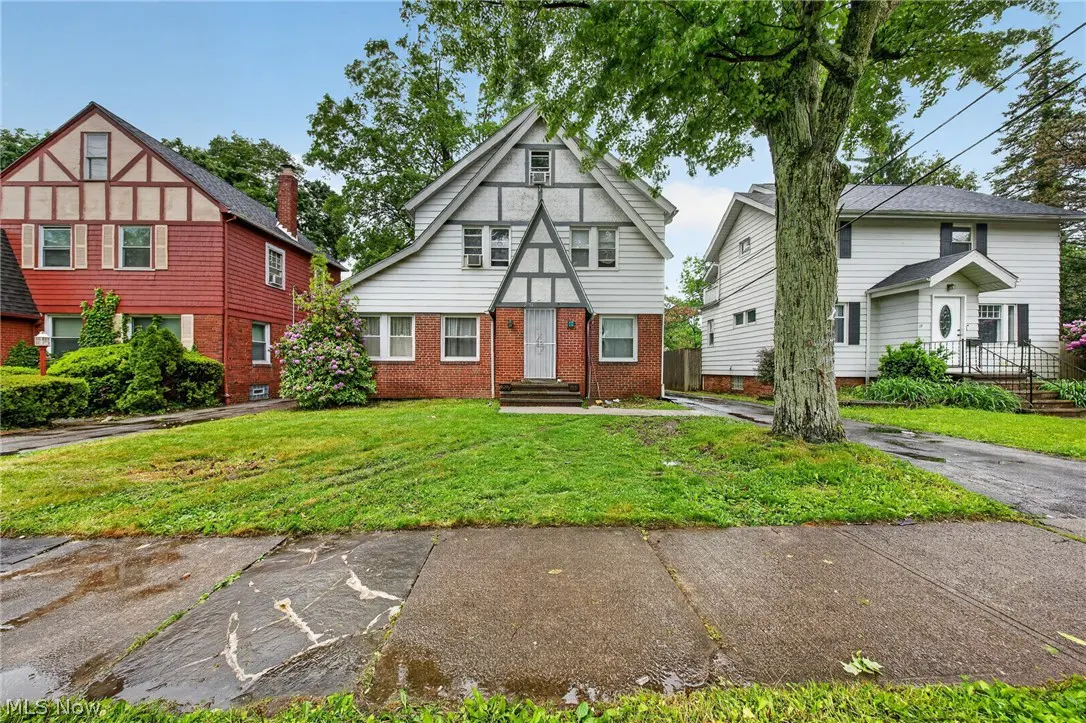 Exterior view of a two-story house with white siding, red brick, and a green lawn on a cloudy day.