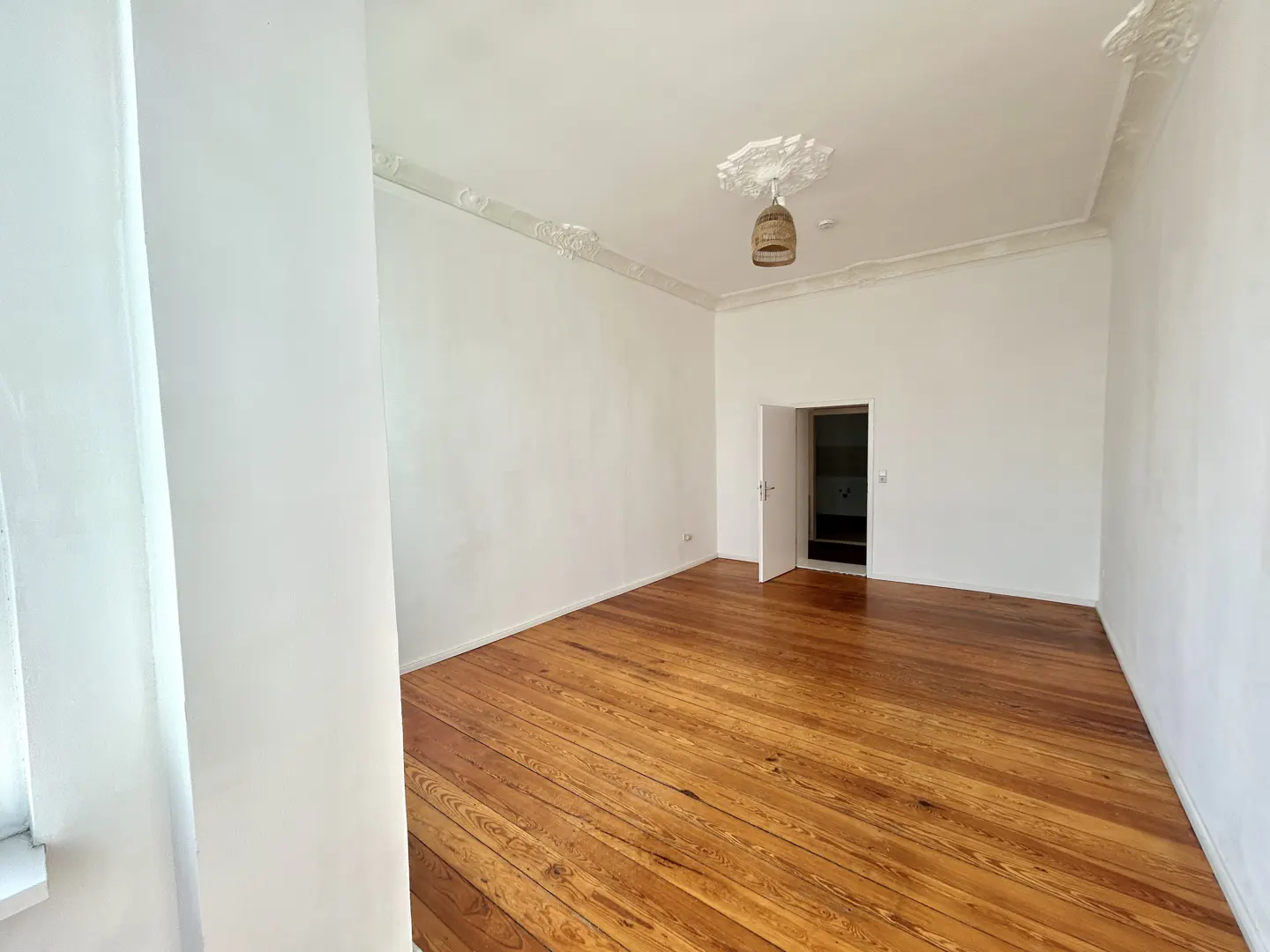 Empty room with hardwood floors, white walls, decorative ceiling molding, and an open doorway to another room.