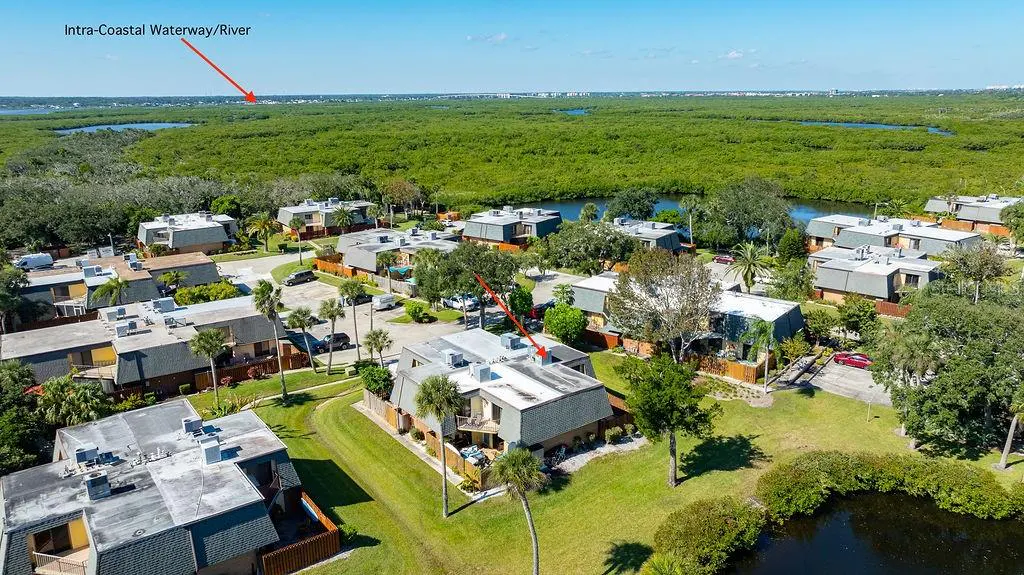 Aerial view of a residential complex surrounded by lush green mangroves and a nearby waterway under a clear blue sky.