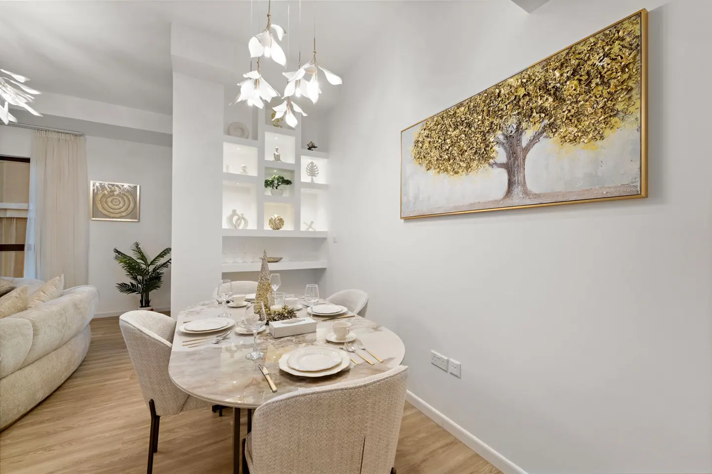 Bright dining room with an oval table set for six, a gold tree painting, and a decorative shelf.