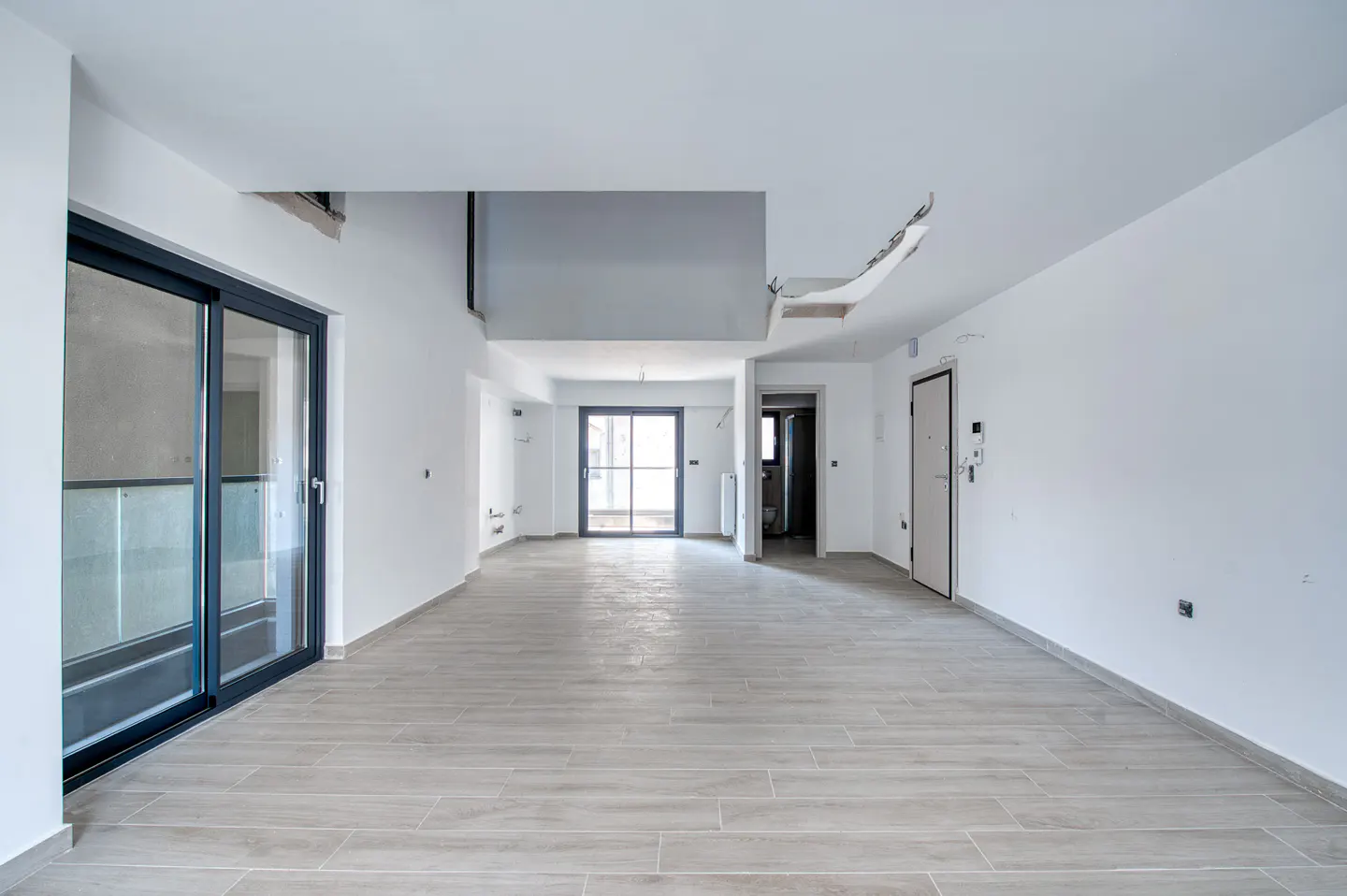 An empty, bright room with white walls, light wood-look tile flooring, and a large sliding glass door.