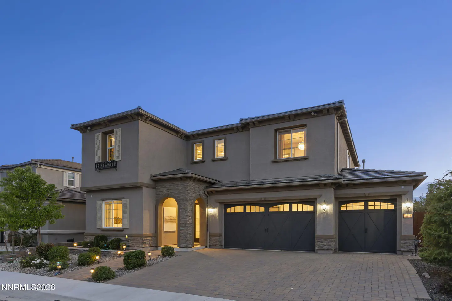 Two-story gray house with a two-car garage, stone accents, and a brick driveway at dusk.