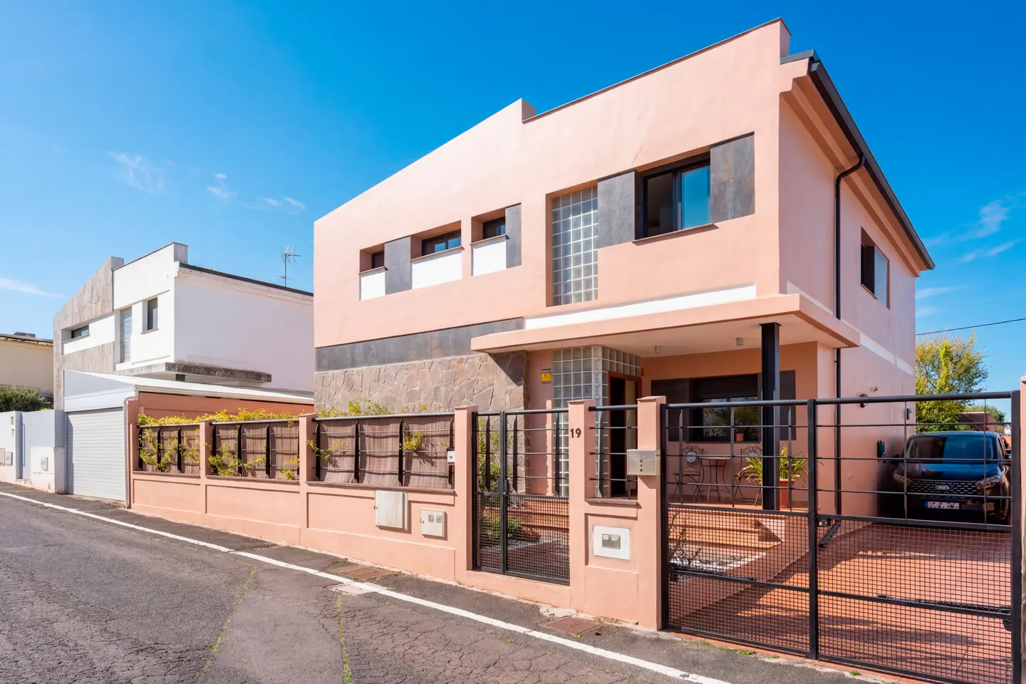 Exterior view of a two-story pink house with a black metal gate and a black car parked in the driveway.