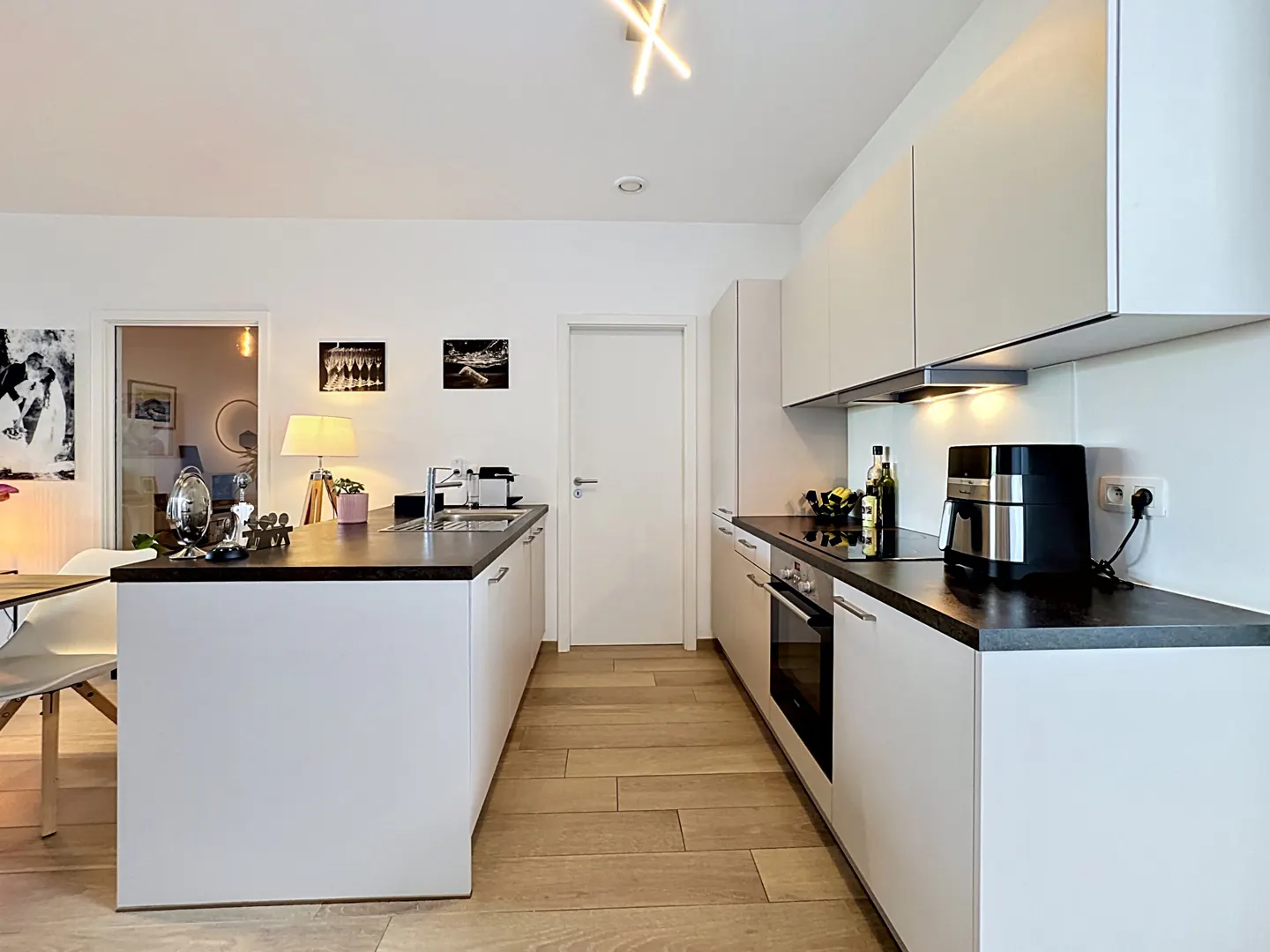 A modern kitchen with white cabinets, dark countertops, and wood floors. A kitchen island is on the left.